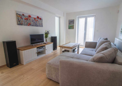Apartmán v přízemí - obývací pokoj s TV, sedačkou a vchodem na terasu